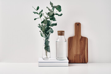 A transparent bottle with a cork stopper, a vase with eucalyptus branches and a wooden board. Natural and eco-friendly materials in interior decor. Copy space, mock up.