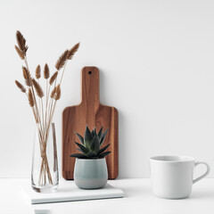 A mug and potted houseplant, a stack of books, a transparent vase and a wooden board. Eco-friendly materials in interior decor, minimalism. Copy space, mock up.