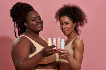 Two young afro female wearing beige underwear and holding bottles of care product