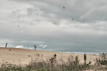 Cloudy sky and sand, in the background a man in a green raincoat. Travel in any weather.