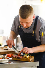 The male chef serves a meat dish and decorates steak. The restaurant's kitchen.