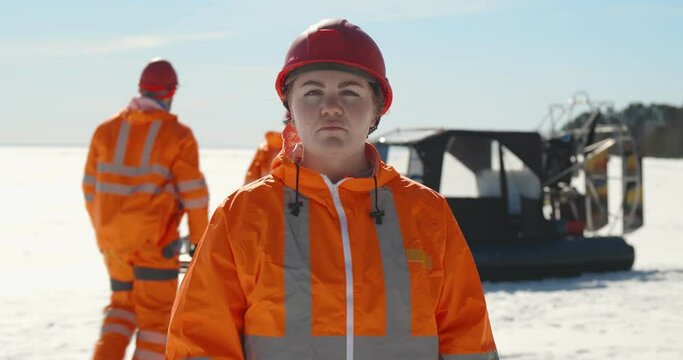 Portrait professional female lifeguard posing at camera while colleagues loading gear in hovercraft