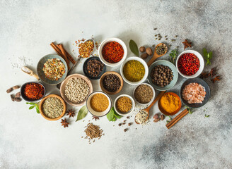 Various dry spices in small bowls and raw herbs flat lay on grey background.