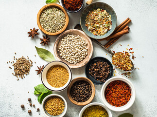 Various dry spices in small bowls flat lay on grey background.