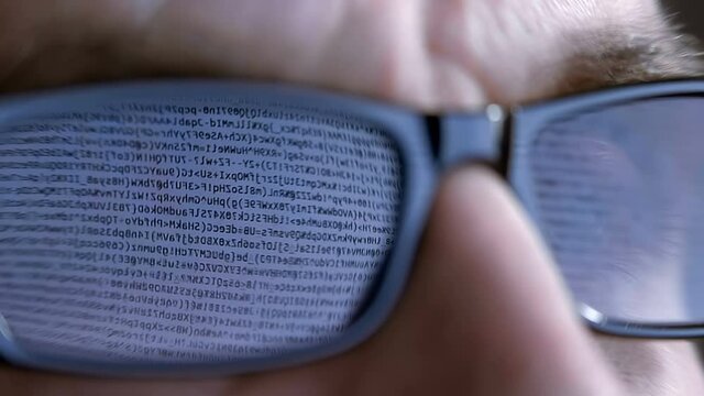 The programmer's (hacker's) glasses reflect the computer program code on which he is working (or trying to hack). Macro. Close Up