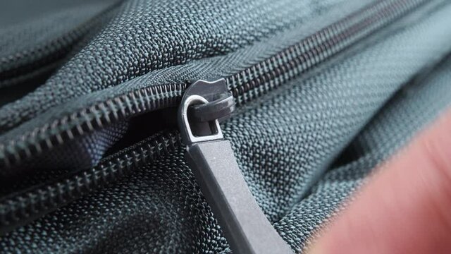 Fingers pull the zipper lock and close the green textile backpack close-up. Macro shooting. Mood travel concept. Selective focus