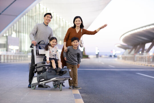 Happy Young Family Waiting For Taxi At Airport