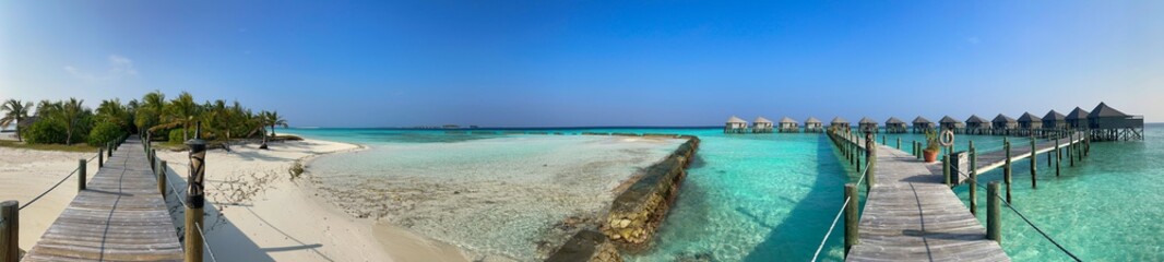 Panorama of Wooden Pier, Palm Trees, Sandy Beach, Lagoon and Water Villa in Maldives. Beautiful View of Maldivian Island Resort Komandoo.
