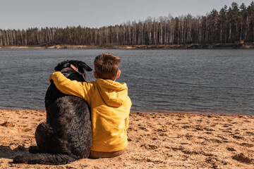 The boy sits on the beach and hugs his large dog labrador breed. Childhood concept. Friendship of...