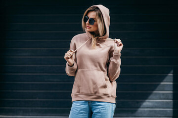 Fasion blonde woman in brown oversize hoodie, glasses and blue jeans, mockup for logo or branding...