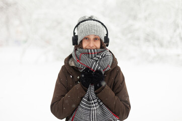 Fototapeta na wymiar Portrait of attractive woman in warm clothes in winter snowy weather outdoors. Listen music in headphones