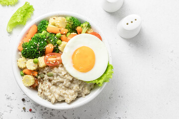 Healthy breakfast savory oatmeal bowl with vegetables and egg. Space for text, top view.