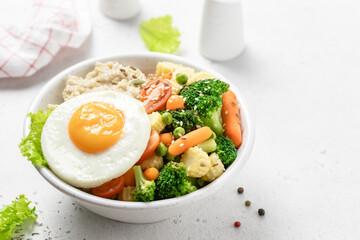 Savory oatmeal bowl with fried egg and steamed vegetables. Space for text.