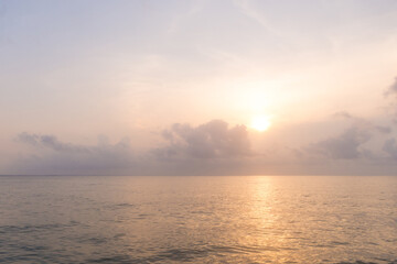 Obraz premium Beautiful view sunrise at morning in the sea and the sun setting behind a cloud creating sparkles and reflections on the water.