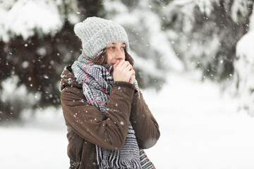 Fototapeta na wymiar Frozen young woman in warm clothes in snowy winter weather in park or forest