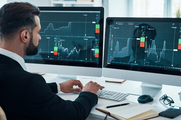 Fototapeta premium Concentrated young man in shirt and tie analyzing data on the stock market while working in the office