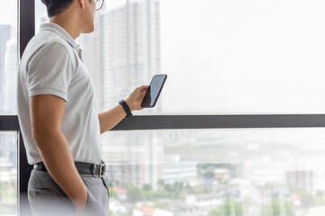 Businessman standing next to big window in modern building looking cell phone.