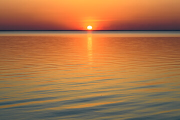 Bright beautiful sunset at the calm sea. Solar disk over water.