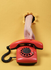 A female hand through a torn hole in yellow paper holds a telephone tube of rotary retro phone. Concept art. Minimalism