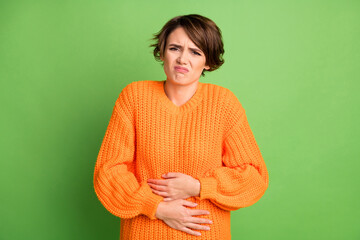 Portrait of sad brunette lady stomach pain wear orange sweater isolated on pastel green background
