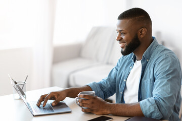 Telecommuting Concept. Young Smiling Black Freelancer Guy Working On Laptop At Home
