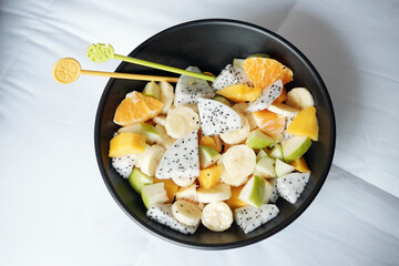 Big bowl of fresh fruit salad on bed and plastick chopsticks