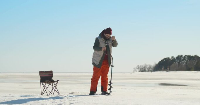 Young fisherman making hole with drill for ice fishing