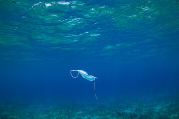 Naklejka premium A surgical face mask that was PPE has been carelessly discarded during the coronavirus pandemic and ended up floating around in the sea where it will harm the environment