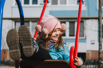 A beautiful, smiling preschool girl, the child is rolling, sitting on a swing, on the playground.