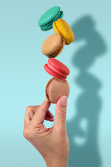 Hand holding stack of colorful French macaroons on light blue background