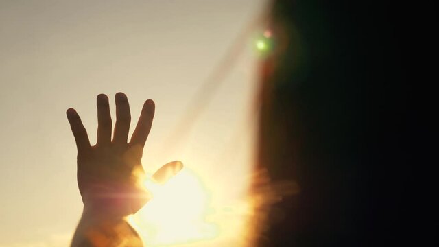 Close-up of a man girl hand at sunrise. hand reaches for the sun against the background of the sky. Sunrise hand silhouette reaching dream. hand girl of a man in the sunbeams of the sky.