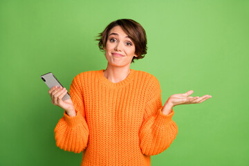 Photo of uncertain young woman shrug shoulders hold smartphone blogger isolated on green color...