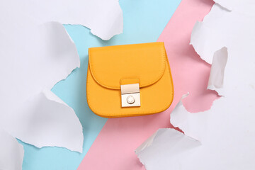 Yellow leather bag on blue-pink background with torn paper. Concept art. Pastel color trend. Top view