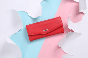 Leather red purse on blue-pink background with torn paper. Concept art. Pastel color trend. Top view