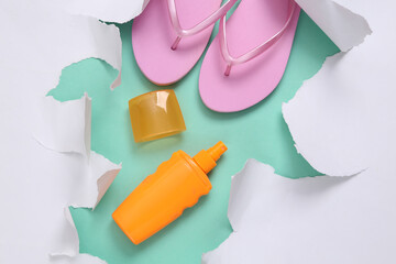 Sunblock bottle and flip flops on blue background with white torn paper. Beach rest Concept. Minimalism. Top view