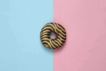 Chocolate donut with icing on a blue-pink pastel background. Top view