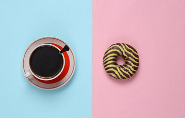 Chocolate donut and a cup of coffee on a blue-pink pastel background. Top view