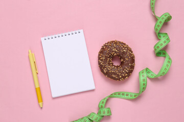 Weight loss plan. Notepad with skipping rope and high-calorie donut on a pink background.