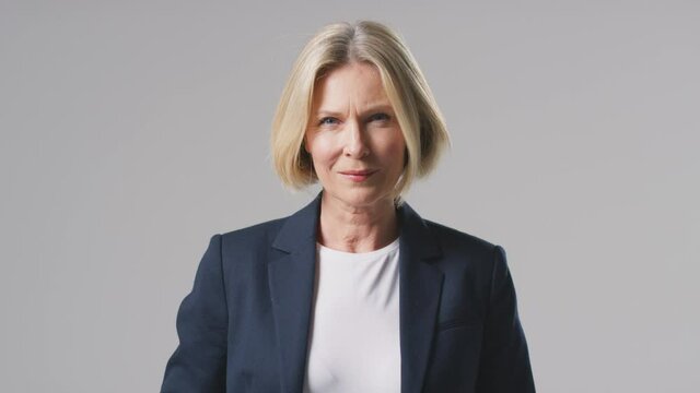 Studio portrait of mature businesswoman with a serious expression against grey background wearing business suit looking at camera - shot in slow motion