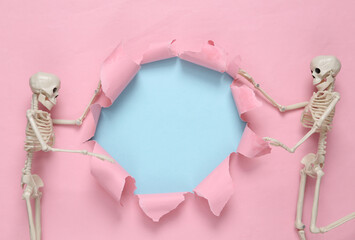 Empty torn hole and skeleton on a blue-pink pastel background. Halloween Concept. Pastel color trend. Minimalism