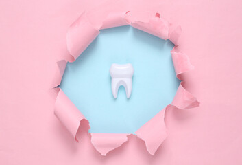 Toy tooth through torn hole on blue-pink pastel background. Concept art. Pastel color trend. Minimalism