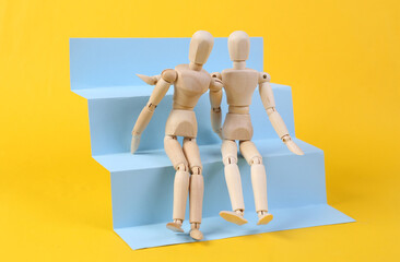 Two Wooden puppets hug on stairs podium, yellow background. Concept art, minimalism