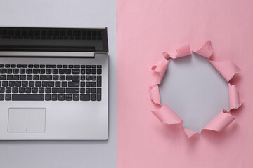 Laptop on pink background with torn hole. Copy space