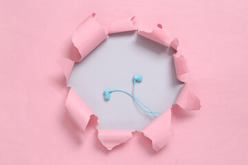 Earphones through the ripped hole of pink paper