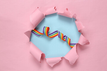 Rainbow lgbt ribbon through ripped hole on pink background