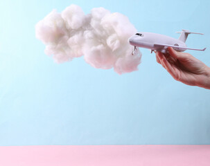 Hand holding Toy air plane with fluffy cloud on pastel blue background. Creative idea. Minimal travel concept.