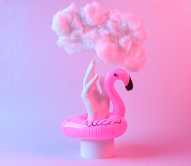Abstract creative composition of inflatable flamingo, hand and soaring cloud in red blue neon light. Minimalism