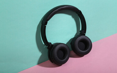 Black stereo headphones on blue-pink background. Minimalism music concept. Trendy shadow. Creative layout.