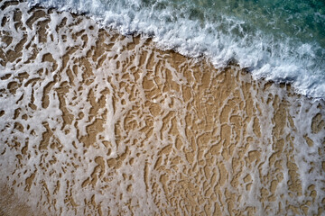Top view of yellow sandy beach with white foam waves.