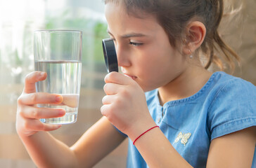 The child examines the water with a magnifying glass in a glass. Selective focus.